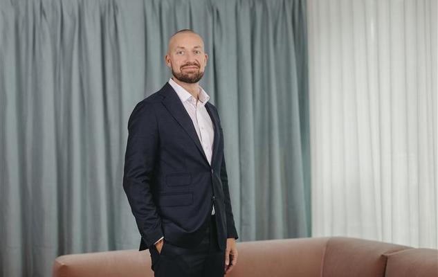 Man i kostym står framför ljus gardinvägg och rosa soffa